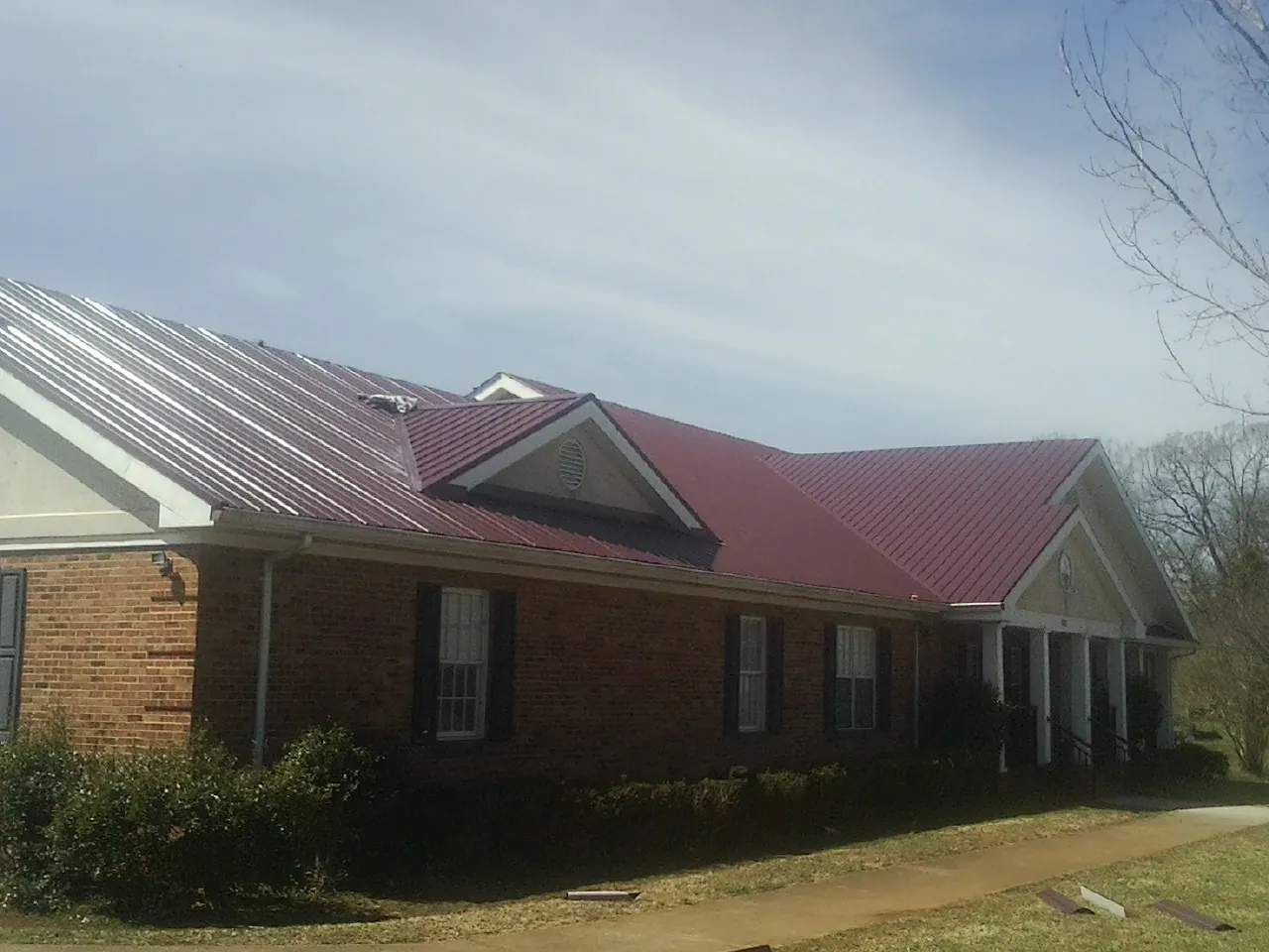 Red metal roof with gabled entries on a long brick building, from a Hail Damage Roof Repair job in Westmoreland City