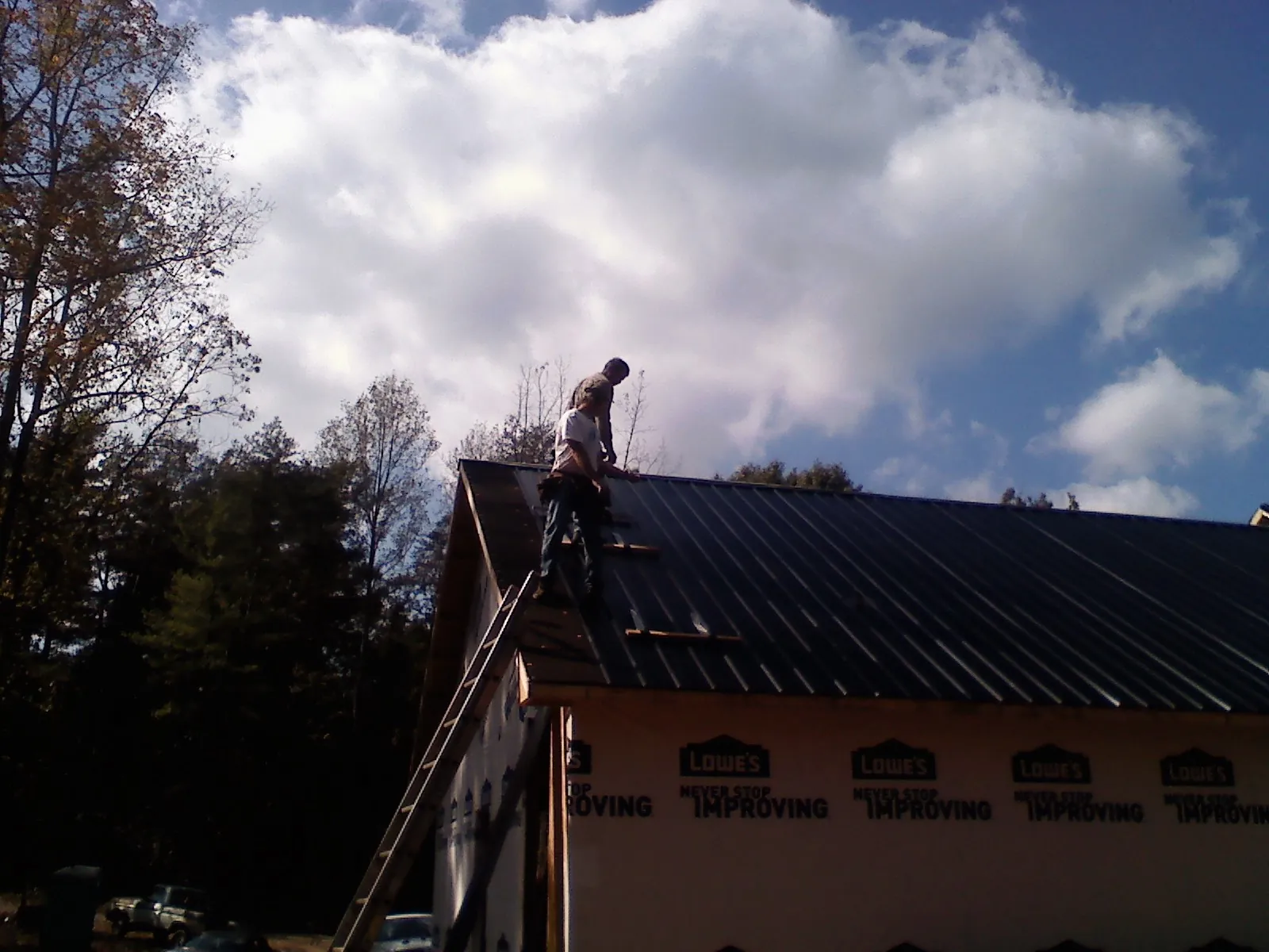 Roofer fastening dark metal panels high against a cloudy sky, from a Roof Inspection job in Westmoreland City