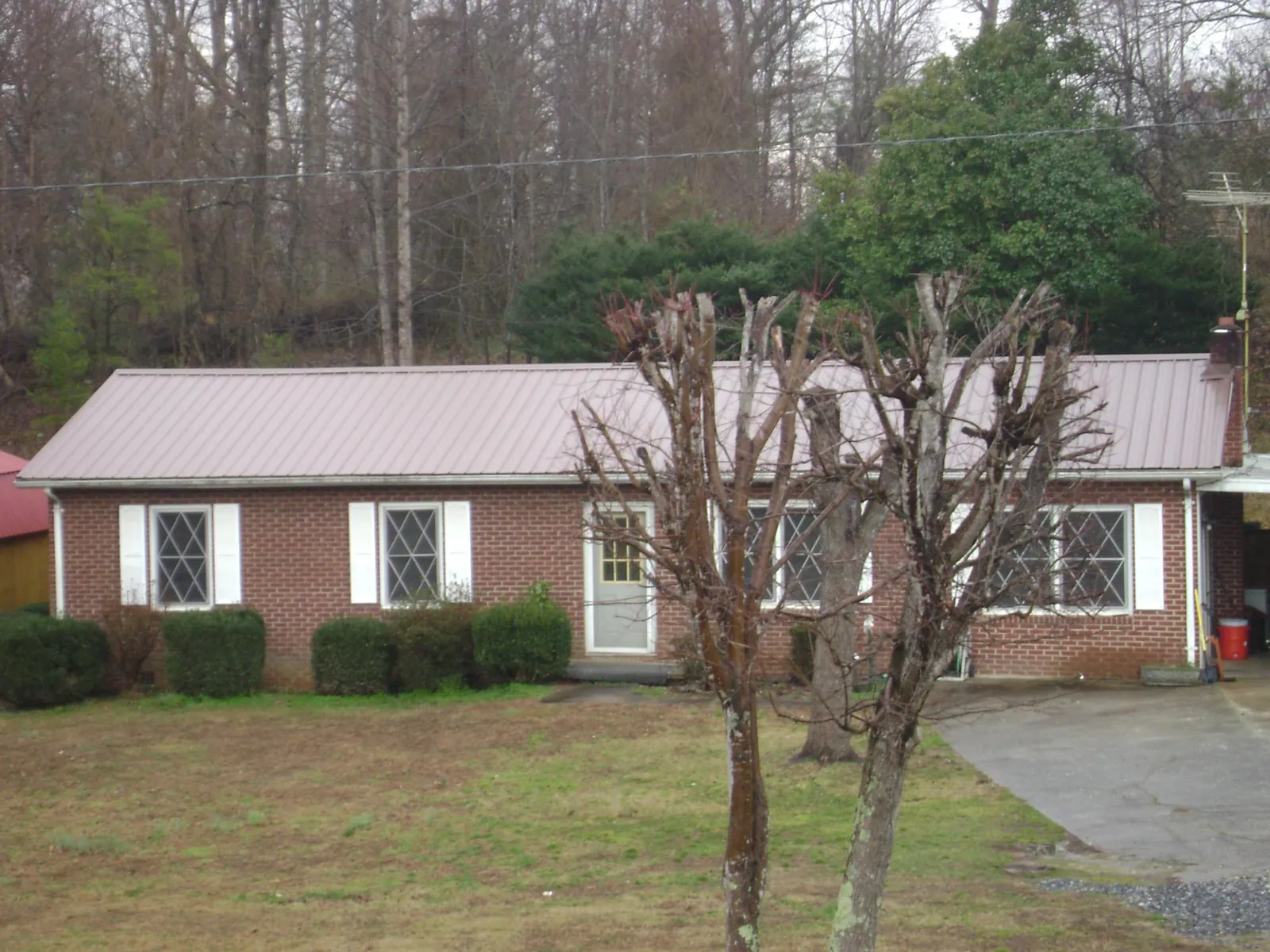Mauve metal roof on a brick ranch home behind bare trees in Westmoreland City