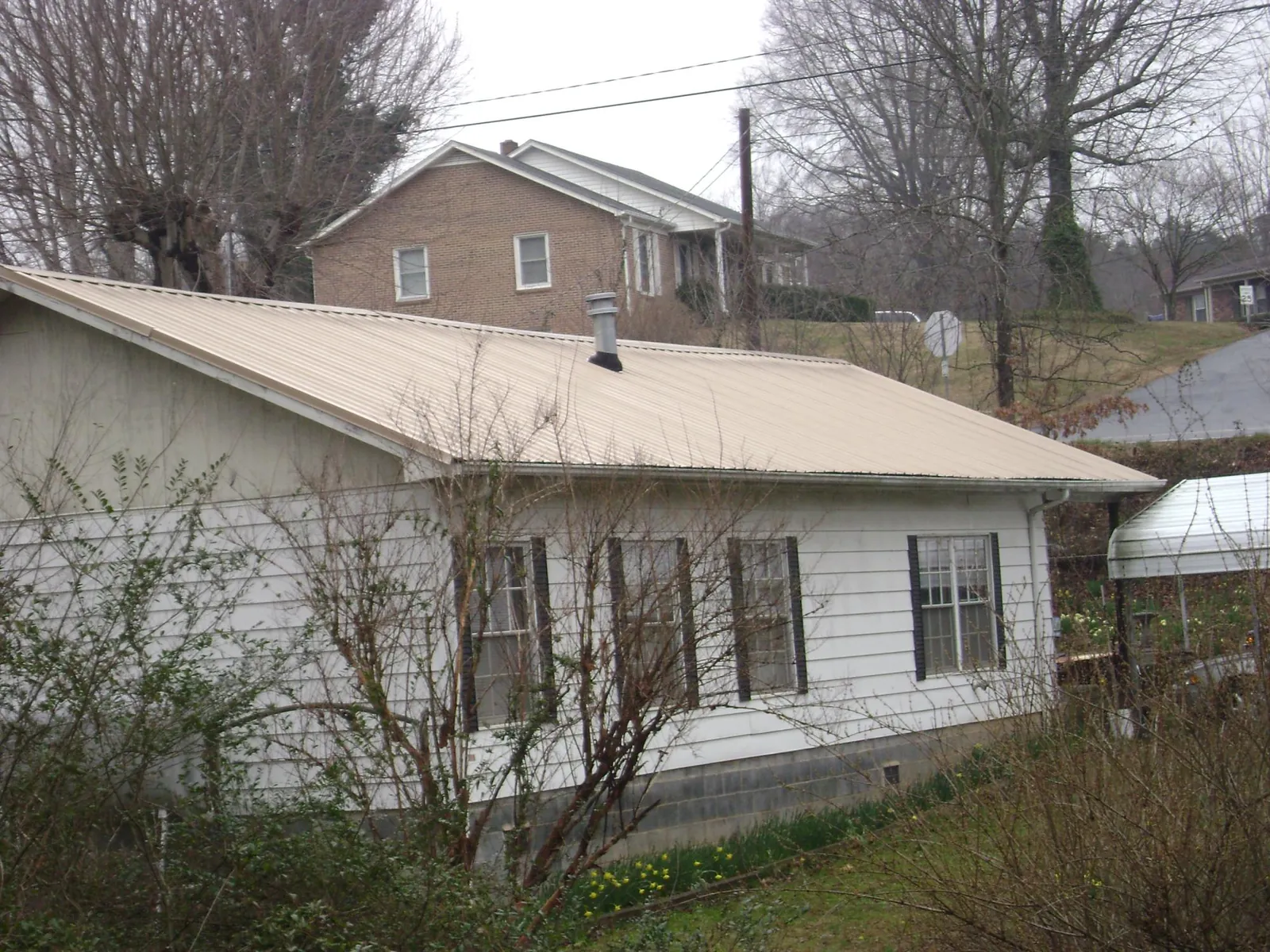 Tan metal roof on a white sided house set into a hillside — Commercial Roofing by Roofing Brothers in Westmoreland City
